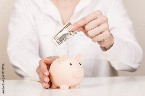 Woman putting dollar bancnote into piggy bank on light blue background, closeup. Space for text photo