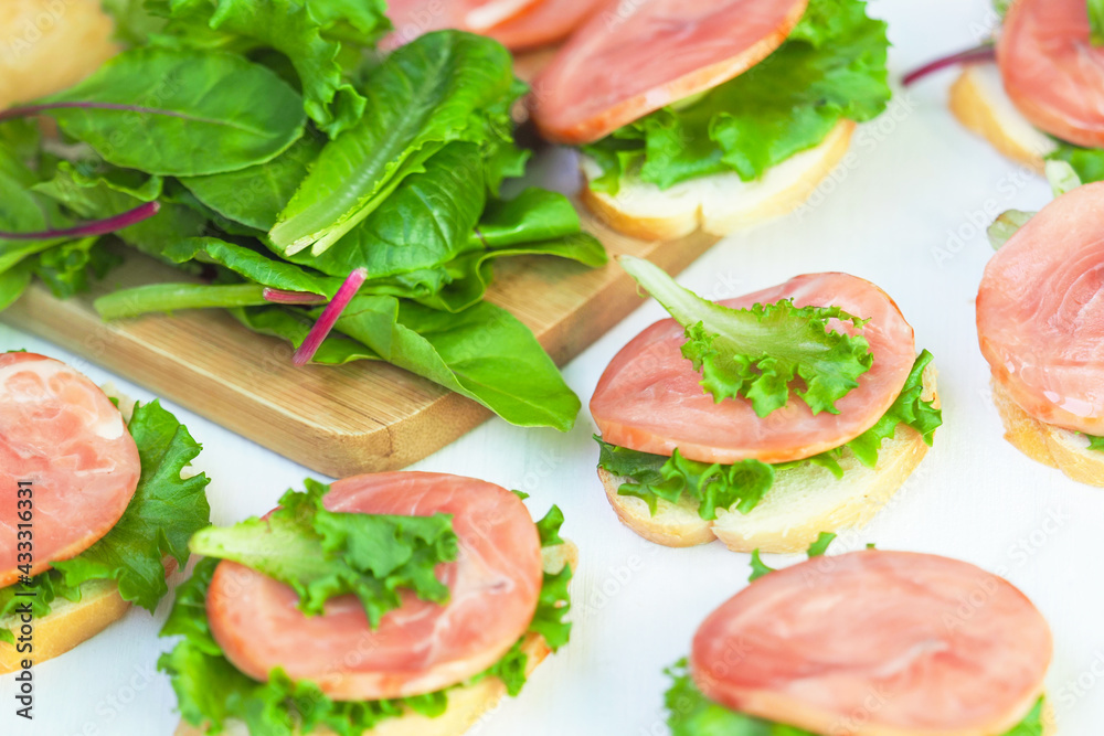 Sandwiches. Cream cheese sandwiches with red fish, baguette, iceberg lettuce leaves, swiss chard on wooden board Sandwiches. Cream cheese sandwiches with red fish, baguette, iceberg lettuce leaves, swiss chard on wooden board
