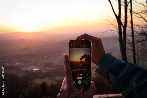 phone holder is trying to take a picture of his fingers holding the sun. Modern technology used to maintain momentum. Pocket little friend for every occasion. Sunset at Beskydy mountains photo