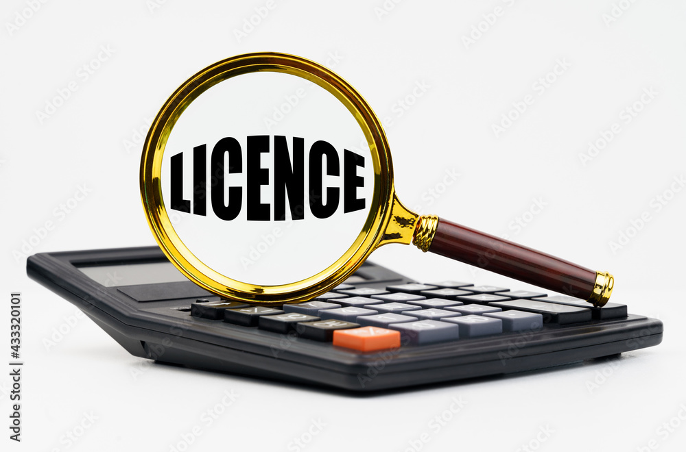 On a white background lies a calculator and a magnifying glass with the inscription - LICENCE On a white background lies a calculator and a magnifying glass with the inscription - LICENCE