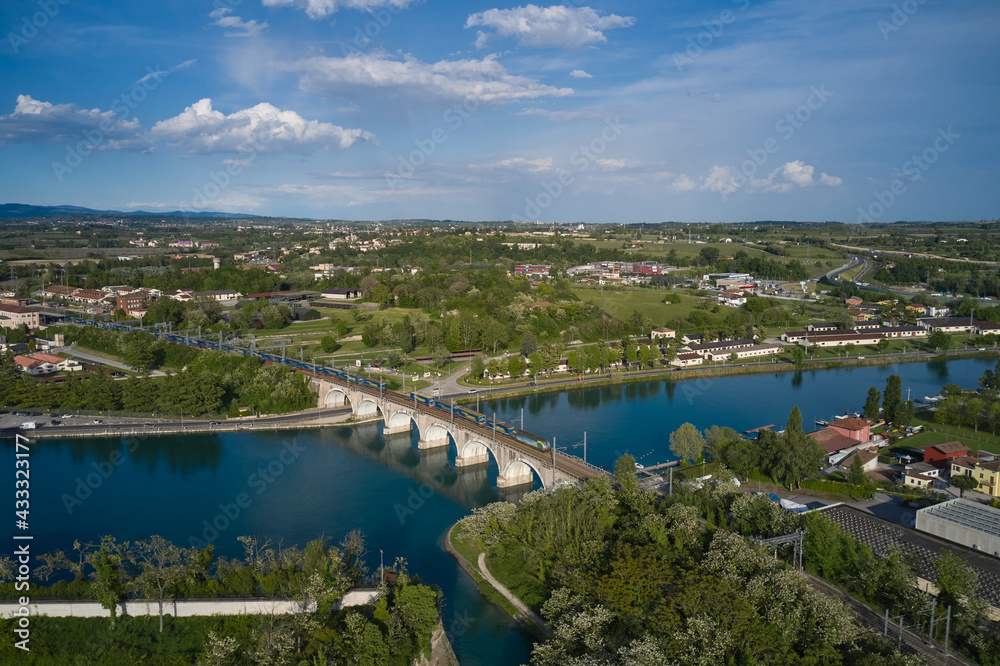 Panoramic aerial view of the train passing over the railway bridge over the river. Peschiera del Garda, Italy. Aerial view of the resort town on Lake Garda.