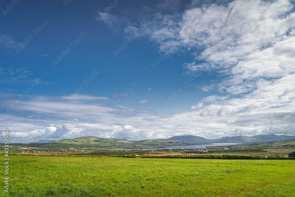 View from Kerry Cliffs on green fields or pasture, mountains and Portmagee village in far distance at beautiful sunny day, Ring of Kerry, Ireland