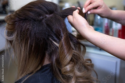 Close up of hands of professional hairdresser in beauty salon curling female hair