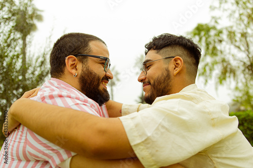 Pareja de jóvenes gay con barba mirándose cara a cara mientras se abrazan 