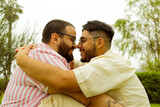 Pareja de jóvenes gay con barba sonriendo y chocando narices mientras se abrazan en el parque