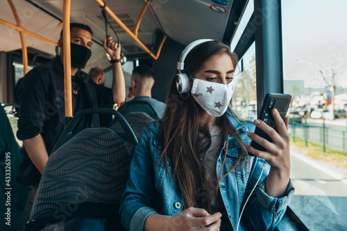 Young woman using a smartphone and wearing protective maskin the bus