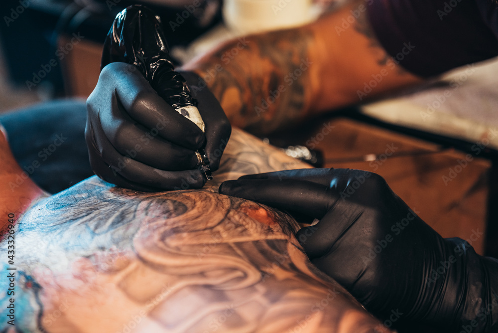 Tattoo artist hands wearing black gloves while holding a machine Stock Photo