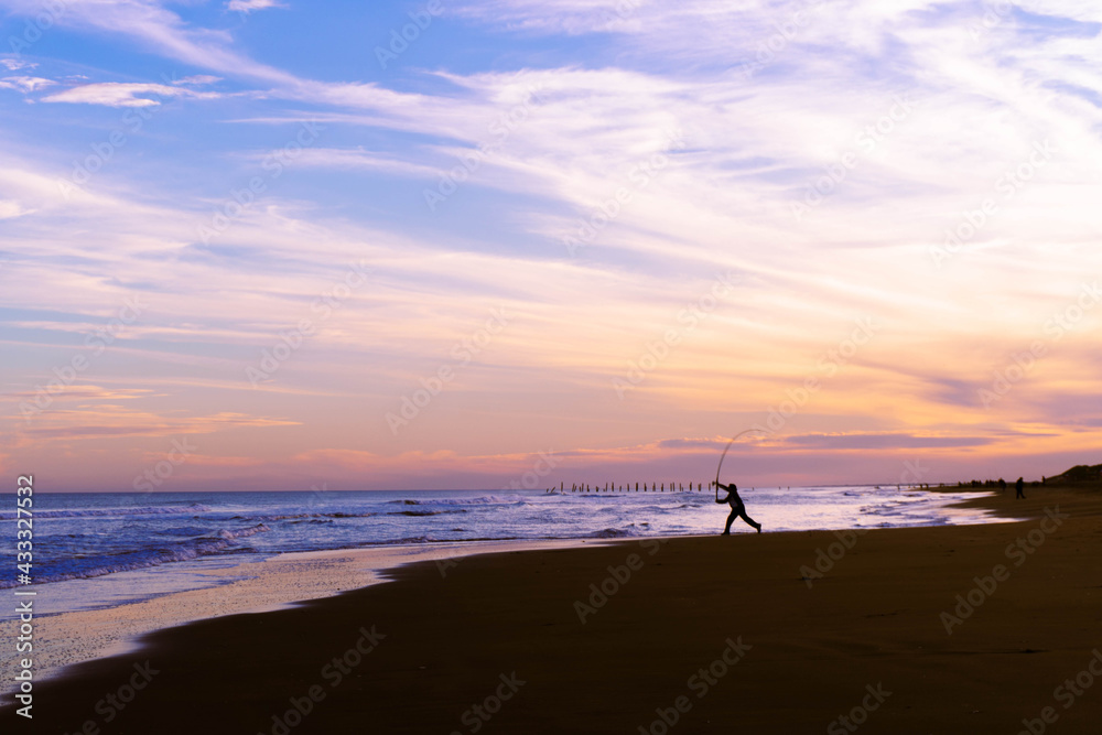silhouette of a person on the beach fishing