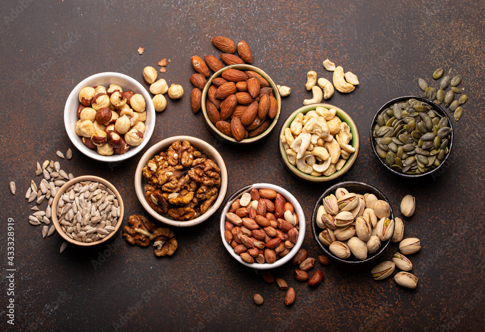 Selection of assorted raw nuts and various seeds in bowls on brown stone background from above, healthy source of energy, fat and vegetarian protein Selection of assorted raw nuts and various seeds in bowls on brown stone background from above, healthy source of energy, fat and vegetarian protein