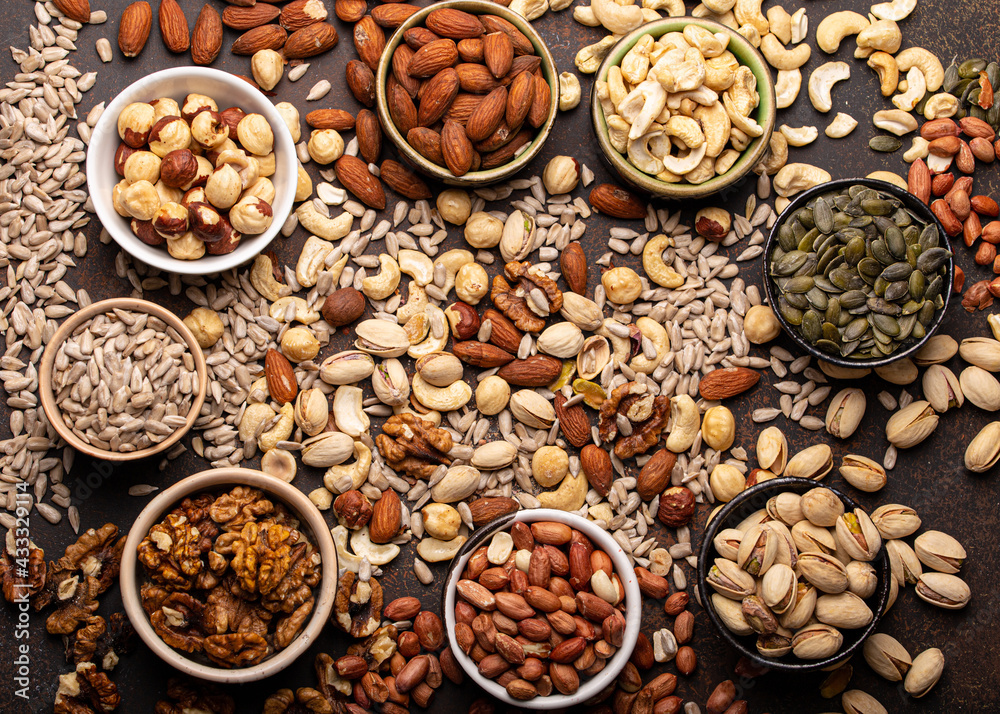 Selection of assorted raw nuts and various seeds in bowls on brown stone background from above, healthy source of energy, fat and vegetarian protein Selection of assorted raw nuts and various seeds in bowls on brown stone background from above, healthy source of energy, fat and vegetarian protein