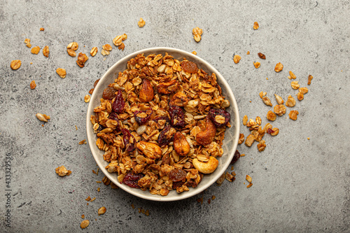 Bowl with crispy homemade granola, healthy breakfast cereal granola with oatmeal, seeds, nuts, berries on rustic stone background from above 