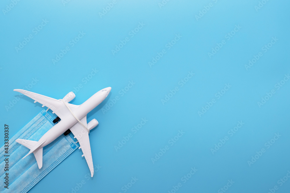 A plane model with a medical mask on a blue background. Safety flight and travel during quarantine and lockdown. Safe travels concept. Opening borders