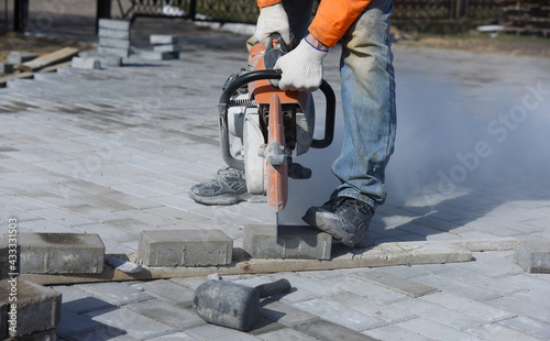 A worker saws a concrete block with a circular saw, laying new paving slabs, building a road.