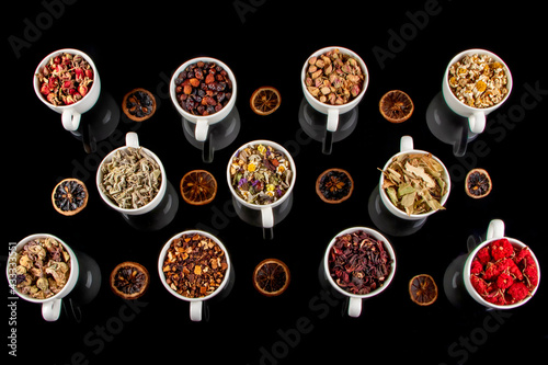 Various kinds of herbal tea ingredients in cups over black background. Natural herbs medicine.