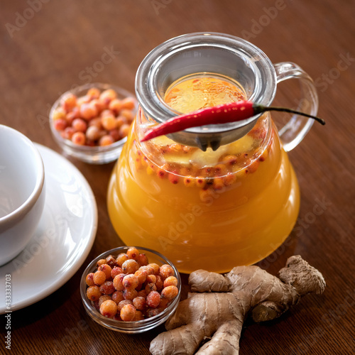 Glass jug of sea buckthorn ginger tea with chili pepper. Hot vitamin drink on wooden table, top view. Healthy lifestyle and eating.