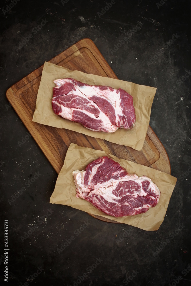 Raw Marbled loin Beef Steaks On Wooden Cutting Board. Sirloin Beef Steaks, Overhead View. Many Raw Striploin Steaks from Marbled Beef on Black Background, Top View.