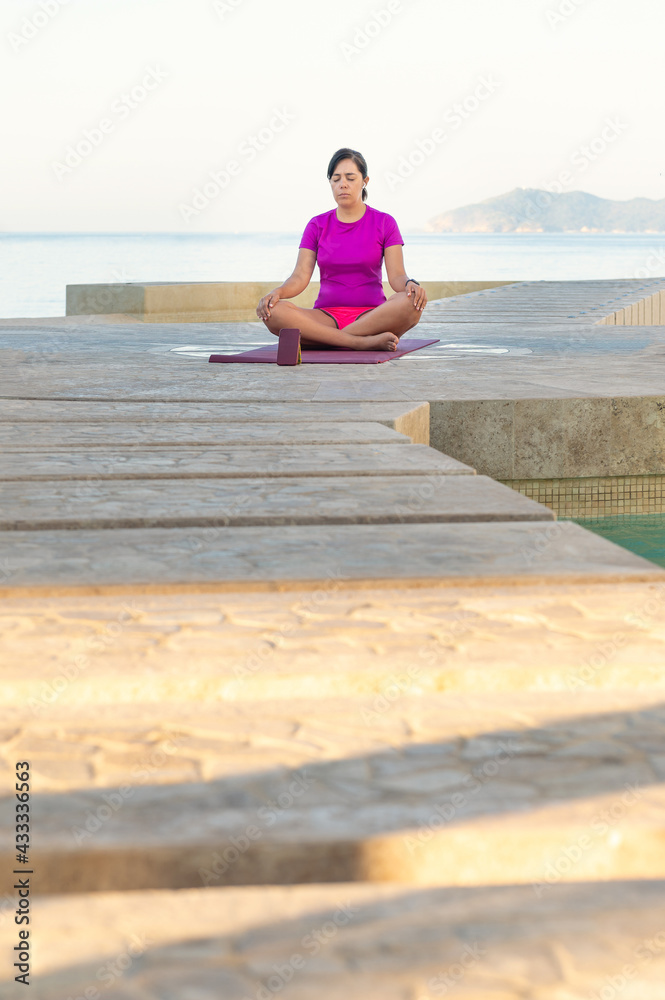 Woman practices yoga in front of the pool. Yoga poses outdoors in front of the sea. Yoga outdoors. Girl doing morning exercise in front of the pool in the pacific ocean. Healthy life concept.