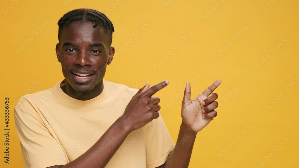 Look at this gesture Joyful black young African American man points his index finger to copy space to advertise your products on yellow background. Advertising concept of promotional offers. Emotions Look at this gesture Joyful black young African American man points his index finger to copy space to advertise your products on yellow background. Advertising concept of promotional offers. Emotions