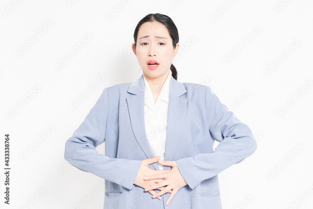 白バックの前に立って、お腹に手を当てる女性 白バックの前に立って、お腹に手を当てる女性