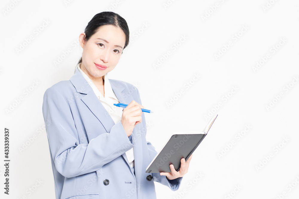 白バックの前に立って、ノートにメモを書く女性
