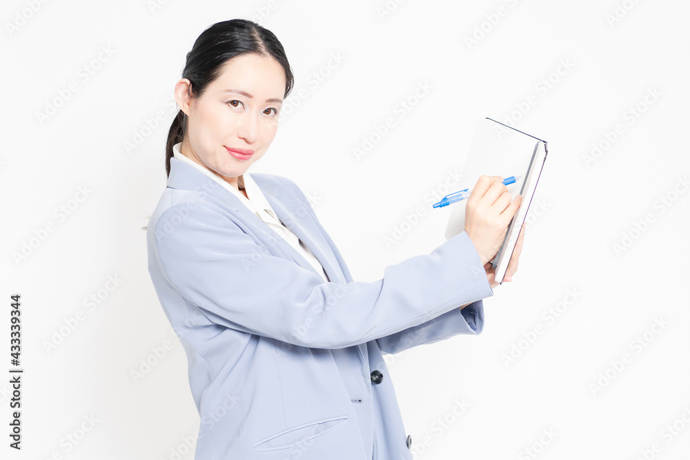 白バックの前に立って、ノートにメモを書く女性 白バックの前に立って、ノートにメモを書く女性