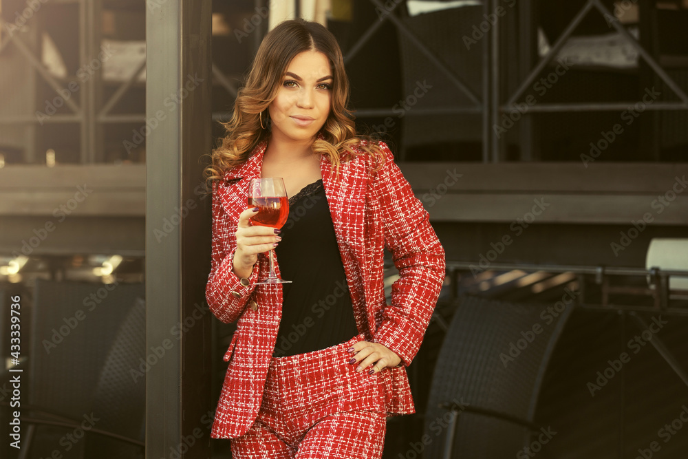 Fototapeta premium Young fashion woman in red tweed jacket and shorts suit at sidewalk cafe