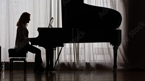 Silhouette of a young musician composing music on the piano, writing notes with a pencil. The concept of writing music