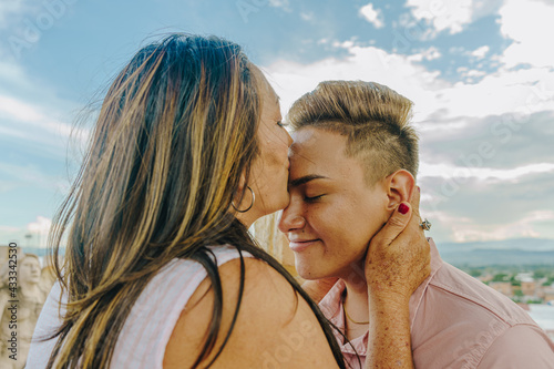 Fotografía Madre besa s u hijo gay en la frente mientras le acaricia el cuello con el cielo