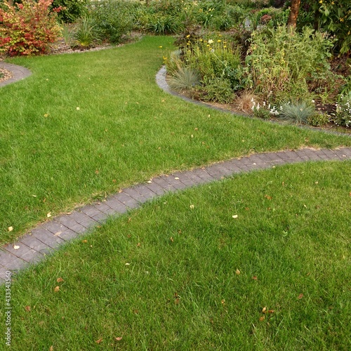 Backyard Garden Modern Design Landscaping. Landscaped Decorative Garden Winding Pathway Or Walkway From Black Bricks. Back Yard Lawn With Curved Brick Paving Path To Country House.