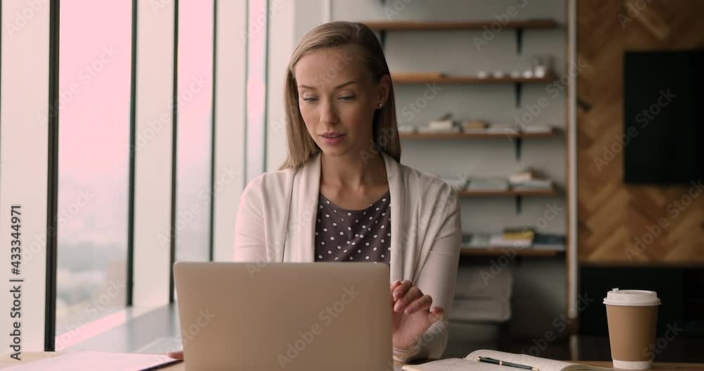 Young office employee work on laptop, taking notes writes down helpful information, do paperwork looking through documents sit at modern workplace desk. Attorney assistant works with contract concept