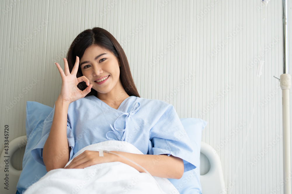 Happy Asian female patient smiling, lies on the bed, and Shows an ok symbol to show confidence in treatment. Concept of believe in treatment And insurance coverage Happy Asian female patient smiling, lies on the bed, and Shows an ok symbol to show confidence in treatment. Concept of believe in treatment And insurance coverage