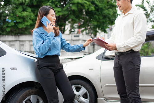 Asian women driver Talk to Insurance Agent for examining damaged car and customer checking on report claim form after an accident. Concept of insurance and car traffic accidents. © Prot
