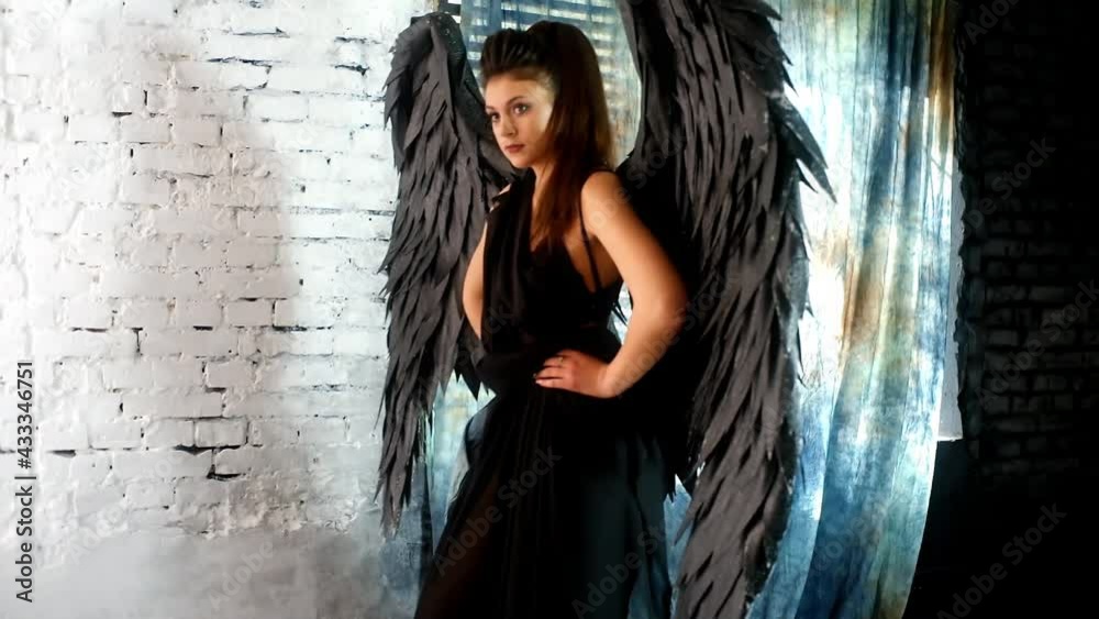 An attractive young sexy woman in a black suit with large angel wings