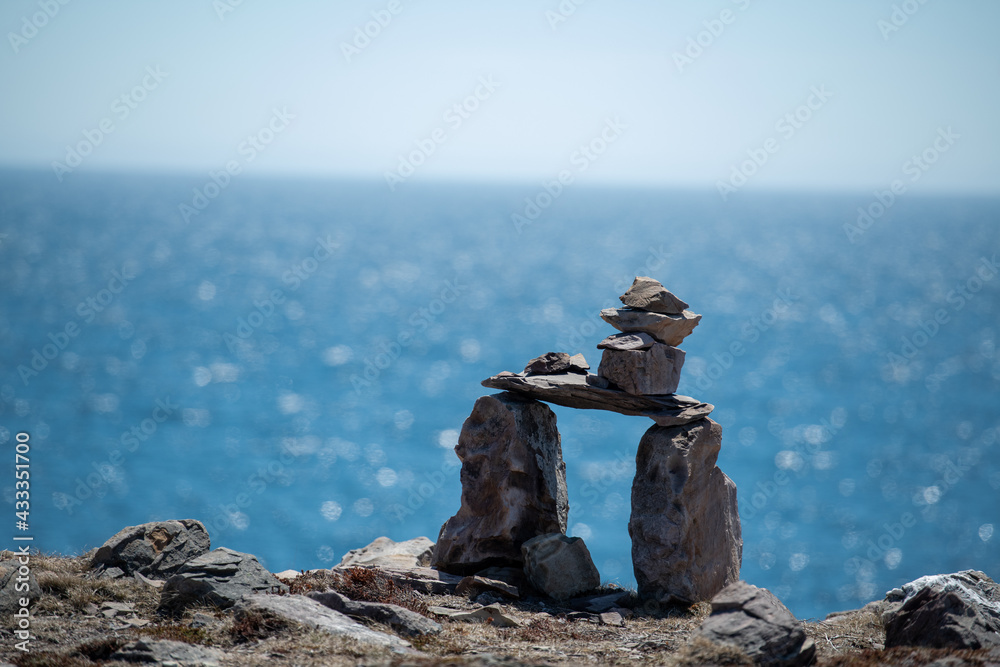 Inukshuk, a stack of granite rocks in the form of a person. The formation is a symbol of direction. The Inuit traditional figure is high on a hill. The background is a blue sky with some clouds. Inukshuk, a stack of granite rocks in the form of a person. The formation is a symbol of direction. The Inuit traditional figure is high on a hill. The background is a blue sky with some clouds.
