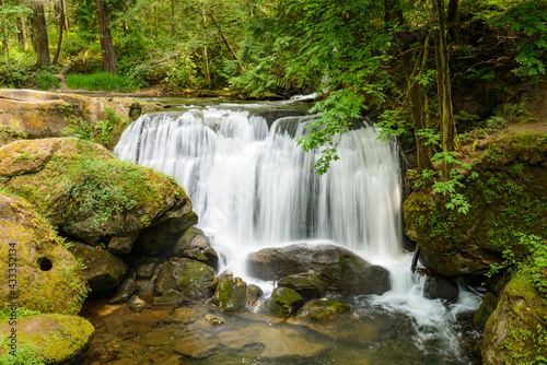 An urban waterfall in Bellingham Washington as Whatcom Falls flows in late Spring over a rocky ledge.  This view is accessible from a bridge in the park