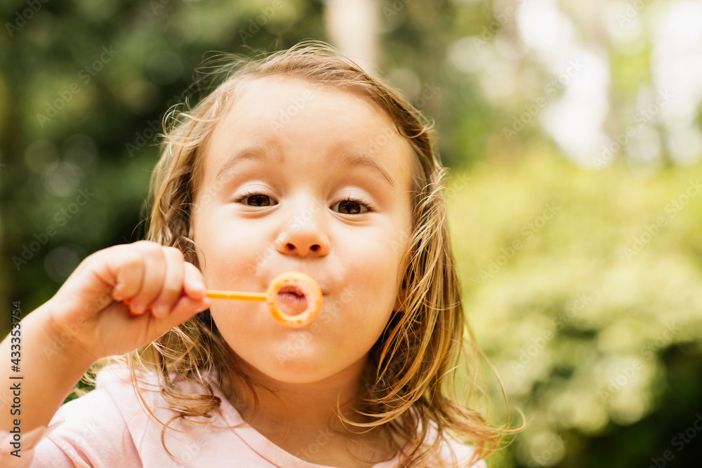 Close up portrait of female toddler blowing bubbles in garden Close up portrait of female toddler blowing bubbles in garden