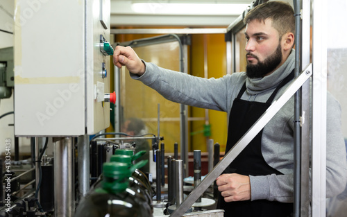 Portrait of skilled guy working on conveyor for bottling olive oil in plastic bottles in small factory