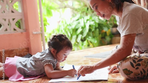 An Asian girl is writing and doing exercises at home with her mother happily in the morning, girl doing activities with her mother on holiday mornings by studying and practicing writing.
