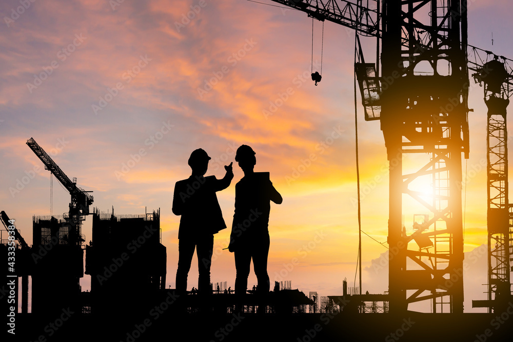 Silhouette of Engineer and worker checking project at building site background, construction site at sunset in evening time
