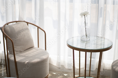 Wooden chairs and cushions with a backrest. There is a table in front of the top is clear glass and a flower vase. All are arranged by the window to let the light come in beautifully 