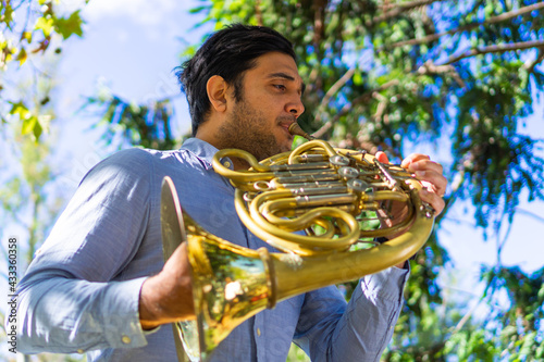 Canvas Print latin man playing a french horn in the park while rehearsing with sheet music