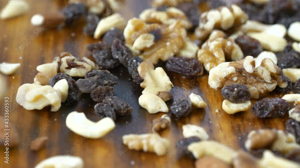 Trail mix with almonds, cashews, pecans and raisins falling onto a cutting board 