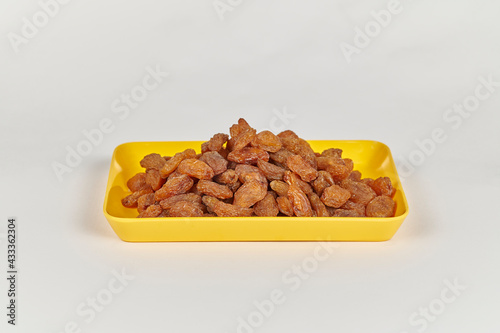 Indian brown raisins (Vitis vinifera) or Munakka on a yellow plate against a white background