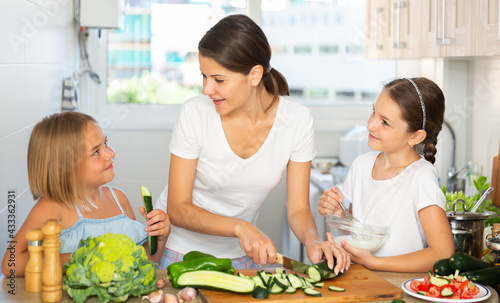 Happy mother with two little daughter cooking vegetable salad at home kitchen