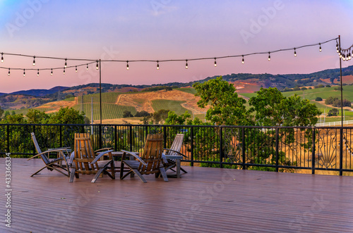 Outdoor al fresco chairs and table on a wooden deck at sunset in the spring with grape vines and hills in the background, Napa Valley, California USA photo