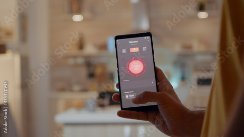 Quadro su tela Young man using smart home application software touching screen to turn on the light by mobile phone