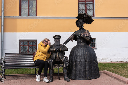 Woman tourist on a bench next to bronze statues in clothes of the last century. photo