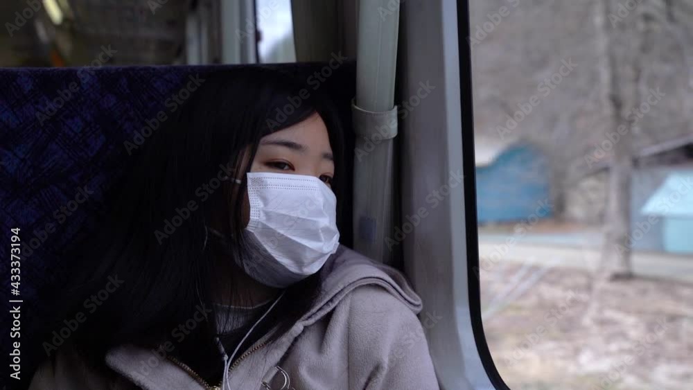 Sad Asian girl wearing facemask looking out from train window at scenery Sad Asian girl wearing facemask looking out from train window at scenery