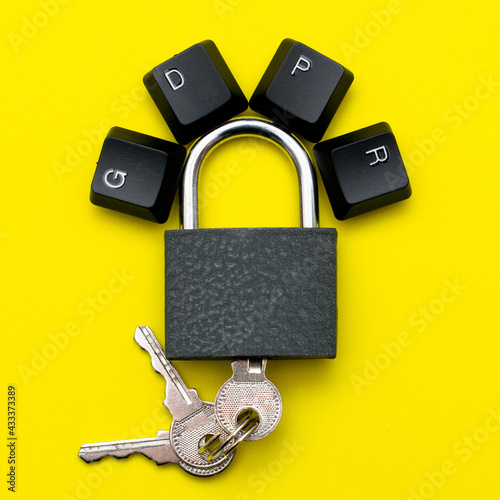 closed iron padlock with keys on a yellow background on the lock lever the keys of the computer keyboard are lined with the abbreviation GDPR the concept of personal data protection