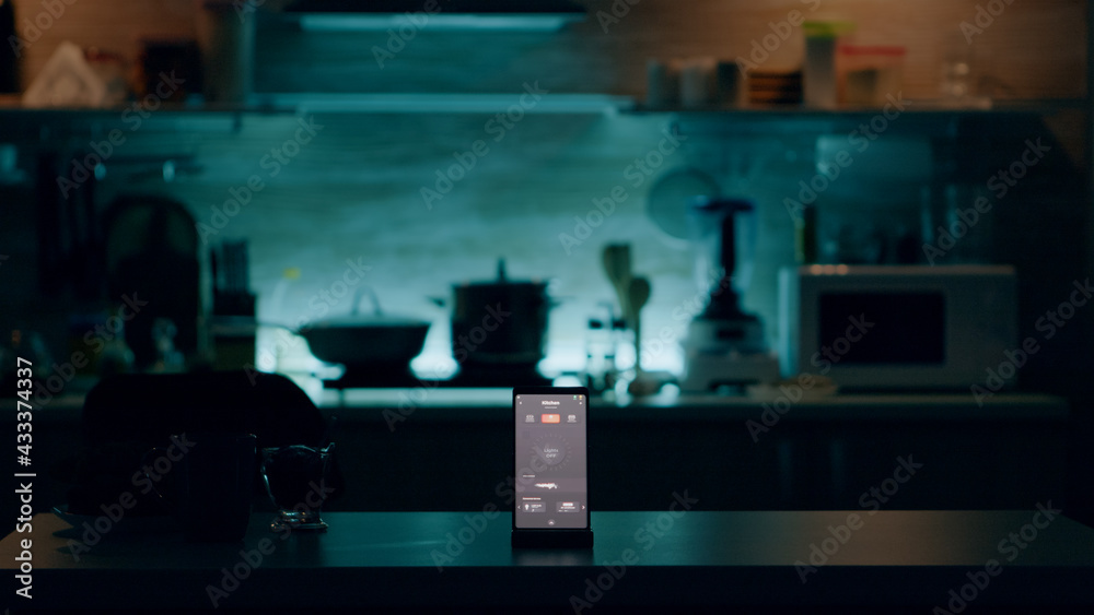Phone with intelligent software placed on table in kitchen with nobody in, controlling light with high tech application. Mobile with smart home app in empty house automation system Phone with intelligent software placed on table in kitchen with nobody in, controlling light with high tech application. Mobile with smart home app in empty house automation system